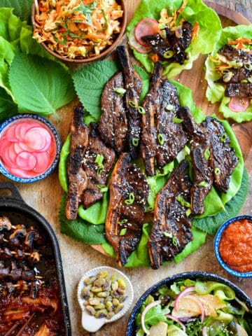 A Korean-Style Barbecue Beef Short Rib Lettuce Wraps spread on a board with coleslaw, salad, grilled mushrooms and kimchi.