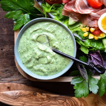 A bowl of green goddess dressing on a platter with a salad.