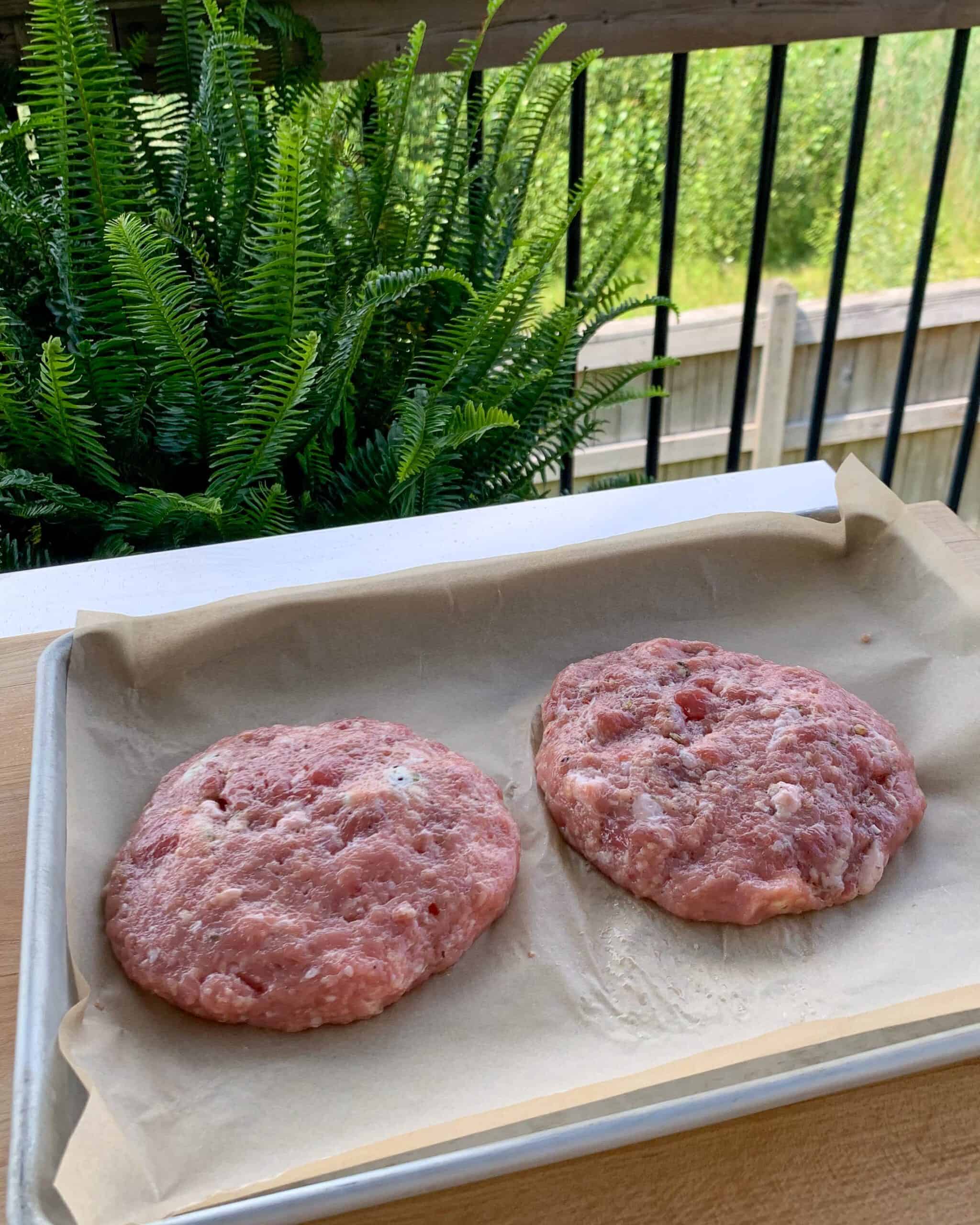 Two turkey patties on a tray ready to be grilled.