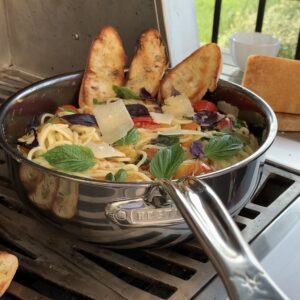 A large pan of cherry tomato spaghetti with garlic toast outside on a grill.