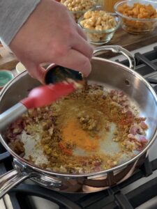 A sauté pan with onions and spices getting added into it.