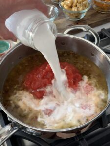 Coconut milk, tomatoes and vegetable stock getting added into the pan.