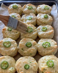 An image of jalapeno biscuits on a sheet pan being brushed with melted butter