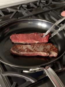 Two steaks in a pan, with one flipped.