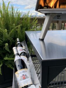 An image of a lit OONI oven with three bottles of Plan Pegau chilling on ice.