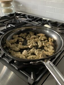 An image of a skillet over a stove cooking chicken.