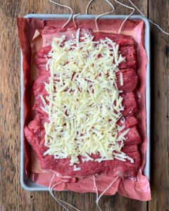 Flattened piece of beef with grated cheese on butchers paper in a sheet pan.