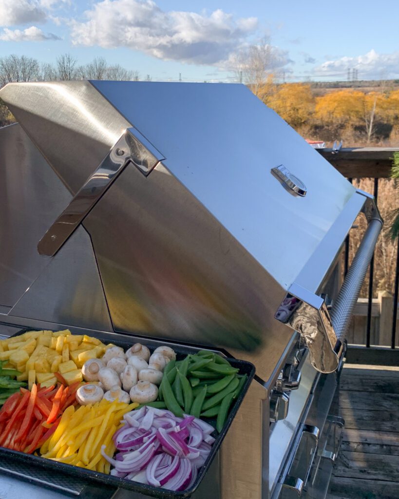 A tray of chopped vegetables sit on the side table on the grill.