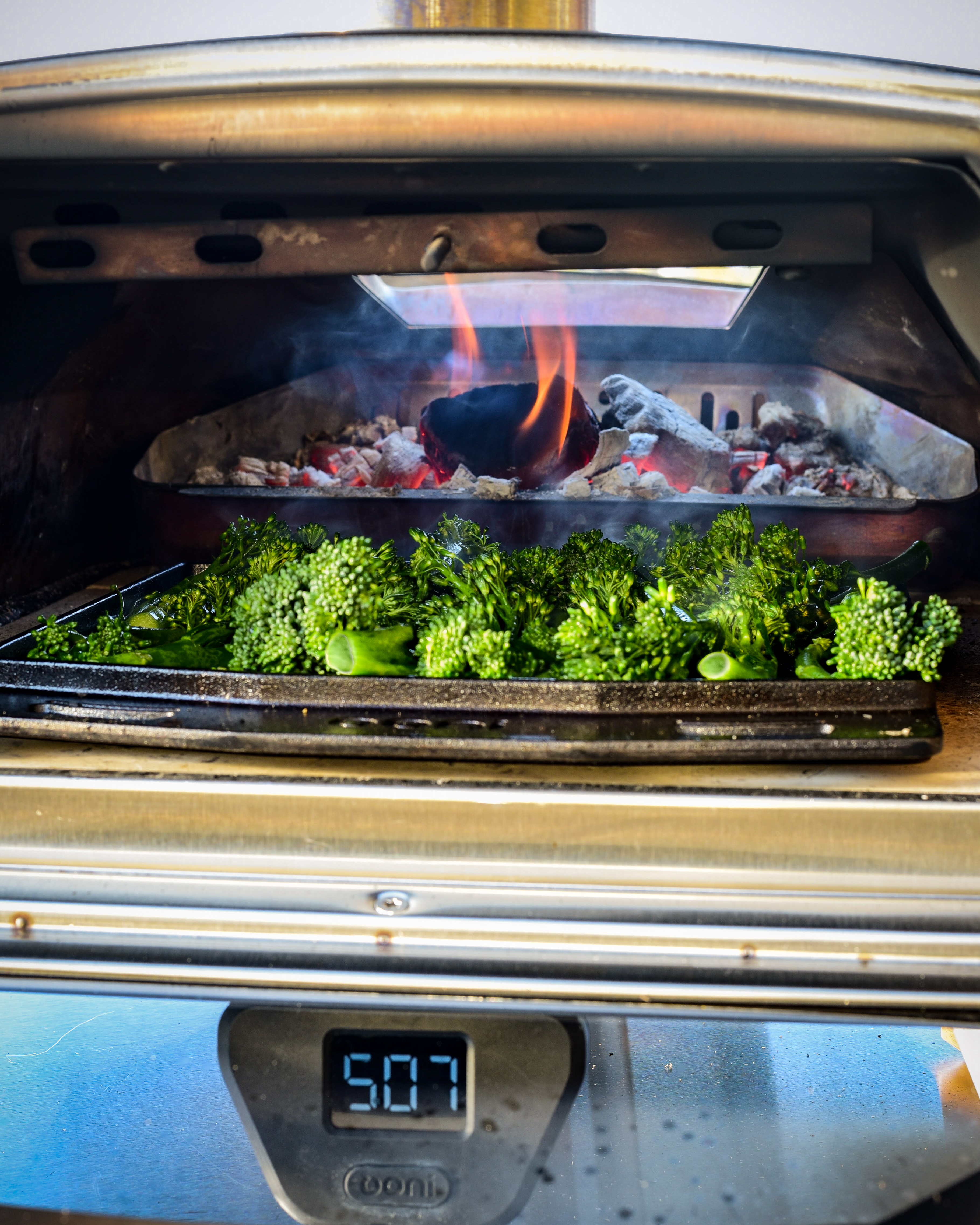 Roasted broccolini on the Ooni grizzler pan in a flaming hot Ooni wood oven.