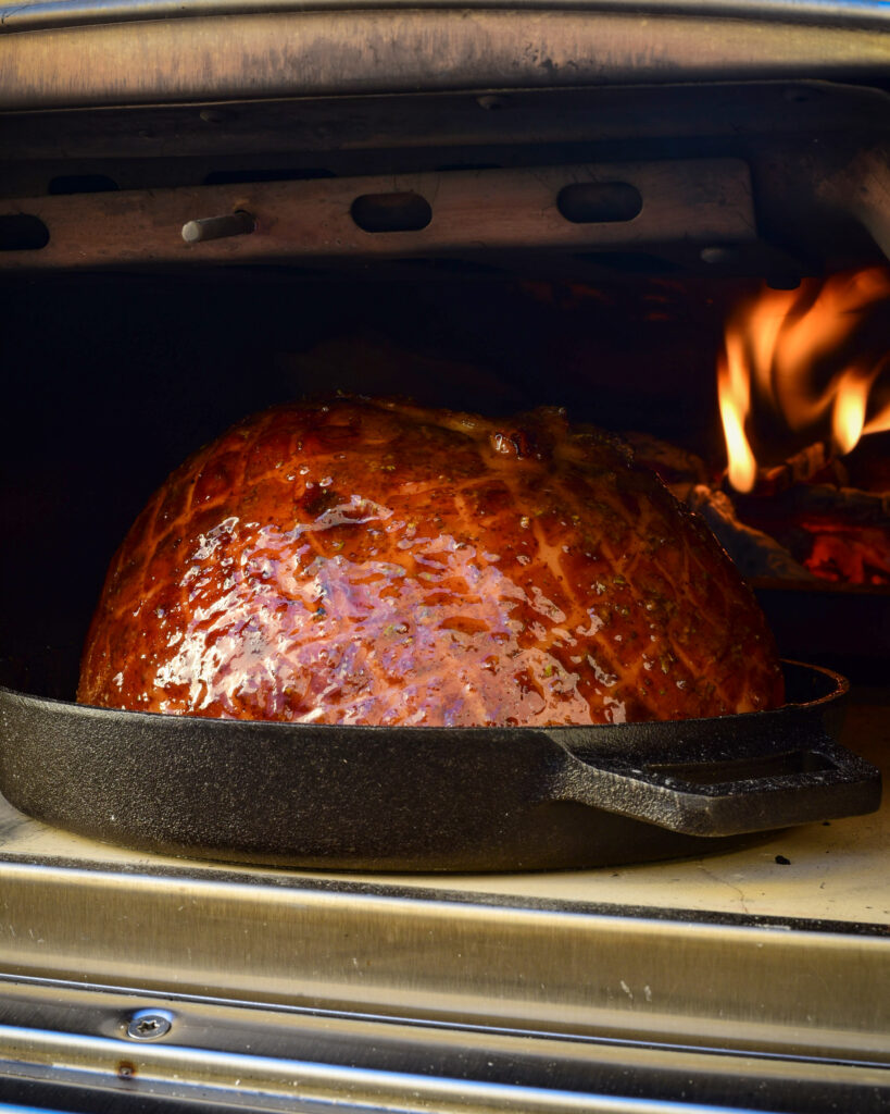 A beautiful glazed and baked ham inside of a flaming outdoor oven.