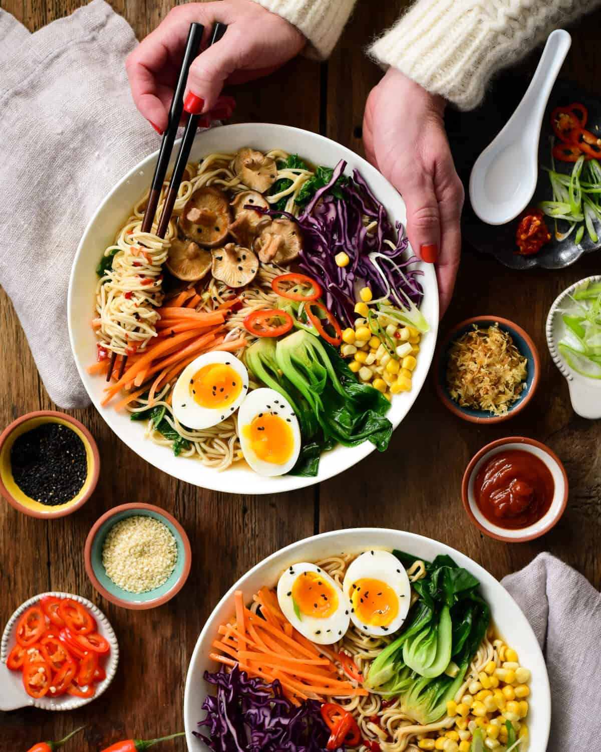 Two colourful bowls of healthy ramen soup, with one bowl being held.
