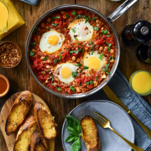 A top down image of a shakshuka with four eggs in a skillet on a table ready to be served.