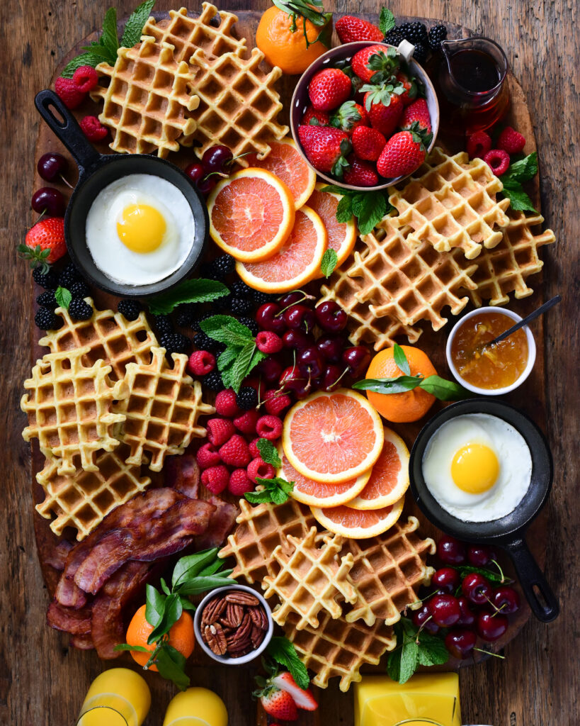 A platter of waffles served with fresh berries, cara cara oranges, thick cut bacon, fried eggs and local maple syrup.