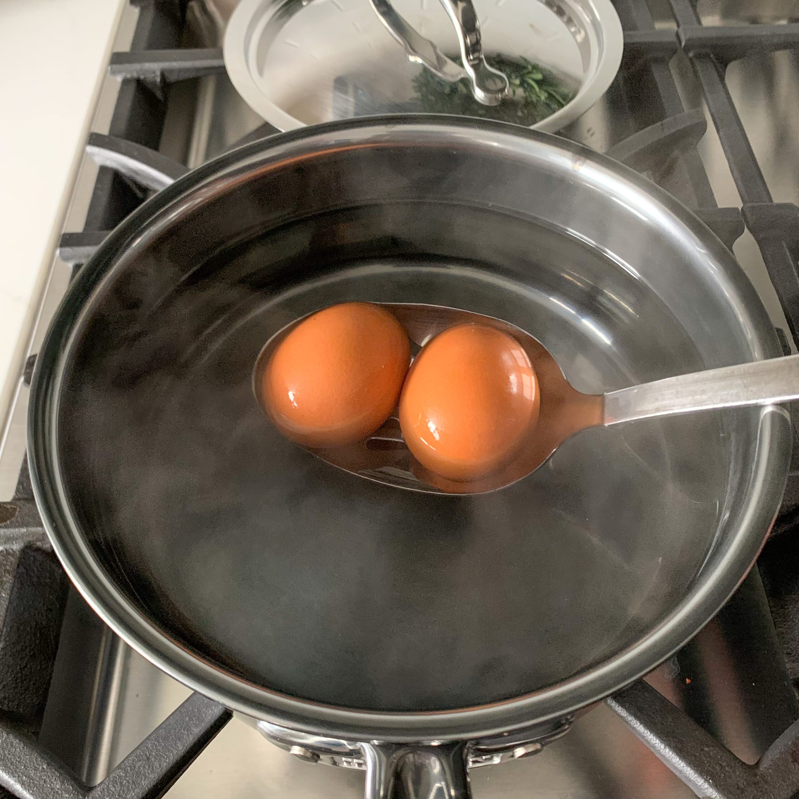 Using a slotted spoon, gently lower the two eggs into the water.