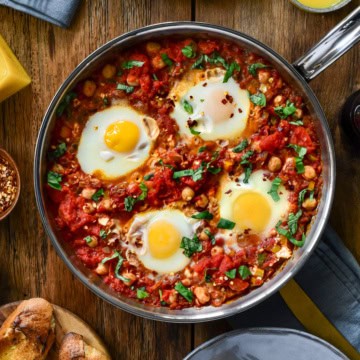 A top down image of a no bake shakshuka with four eggs in a skillet on a table ready to be served.