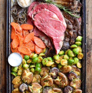 A sheet pan with a roasted vegetables and a prime rib roast sliced to reveal a perfect pink interior.