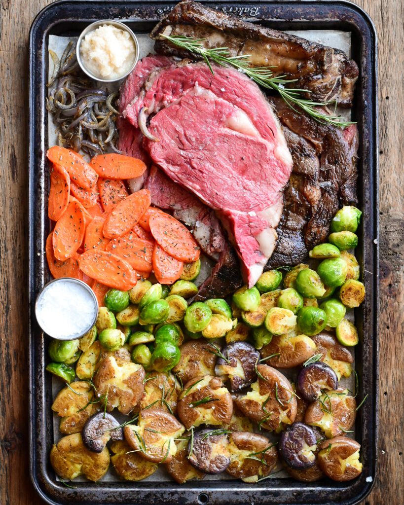 A sheet pan with a roasted vegetables and a prime rib roast sliced to reveal a perfect pink interior. 