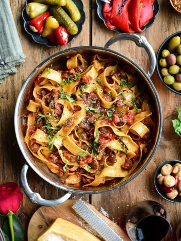 A top down image of a pan filled with pappardelle noodles and a bolognese sauce.