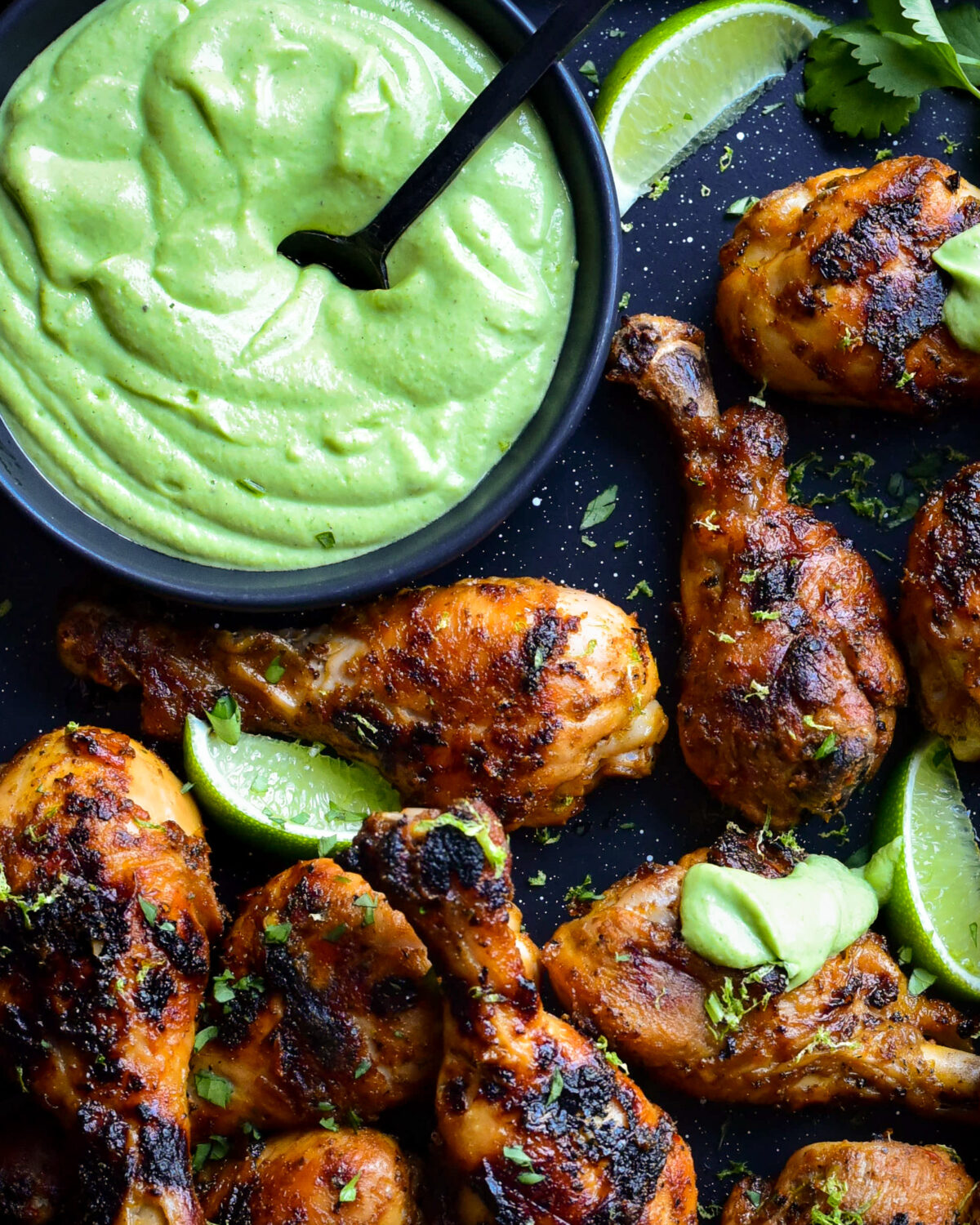 A big bowl of spicy cilantro green sauce served with charred chicken drumsticks and limes.