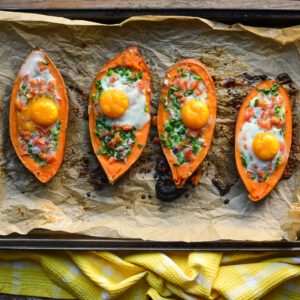 Four sweet potato boats just baked on a baking sheet with veggies and an egg in each boat.