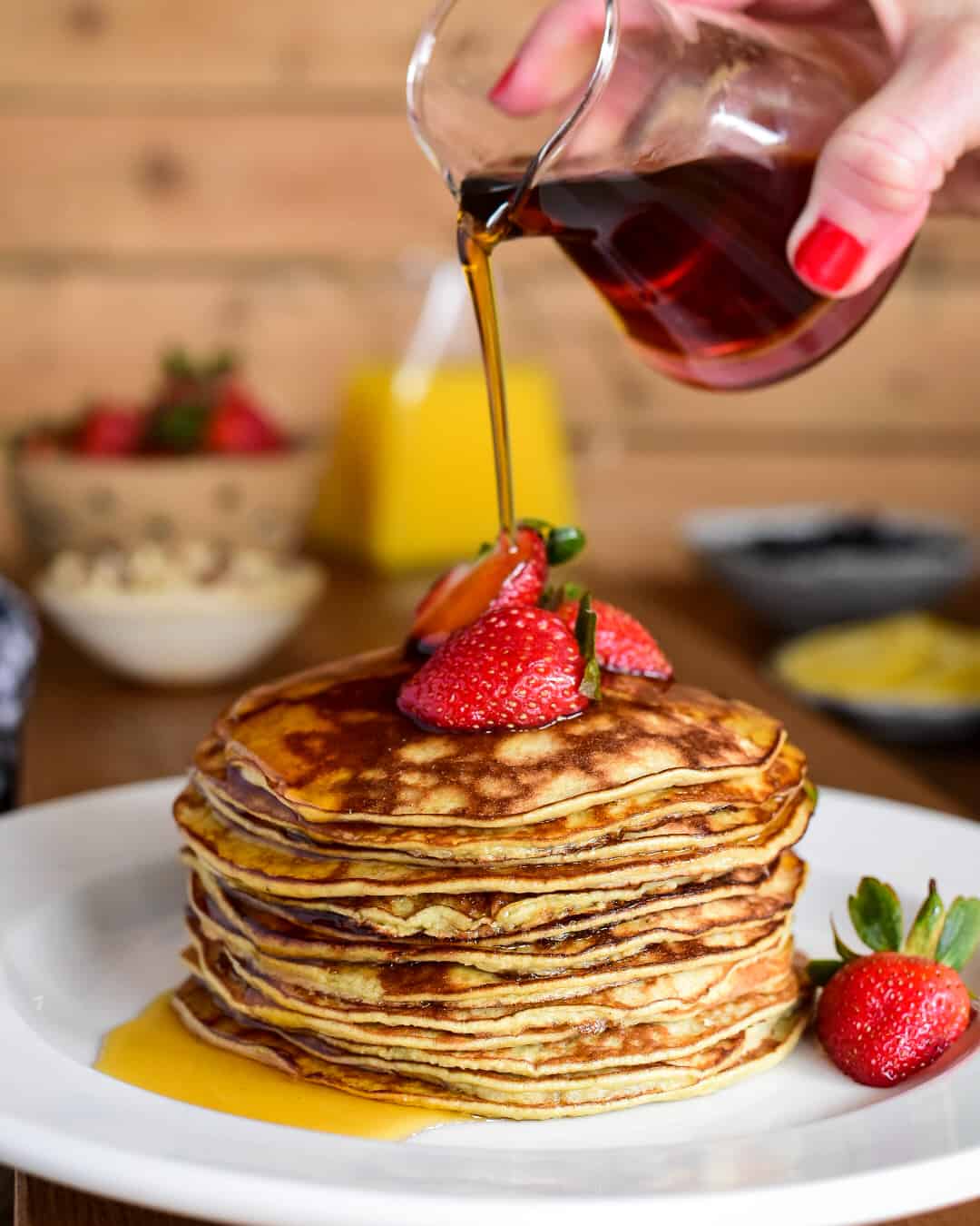 Two Ingredient Banana Pancakes - stack with strawberries and a stream of pouring syrup.