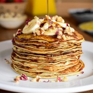 Two Ingredient Banana Pancakes - stack with bananas and walnuts and a stream of pouring syrup.
