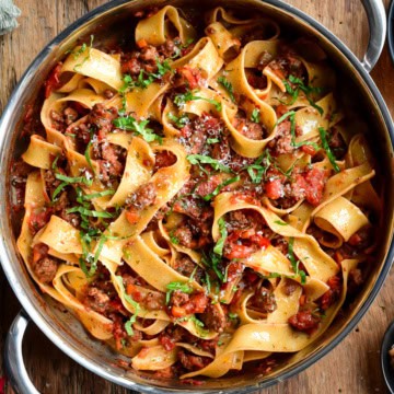A top down image of a pan filled with pappardelle noodles and a bolognese sauce.
