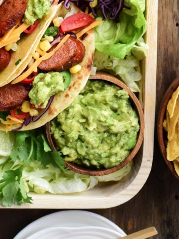 A bowl of spicy guacamole on a platter of tacos