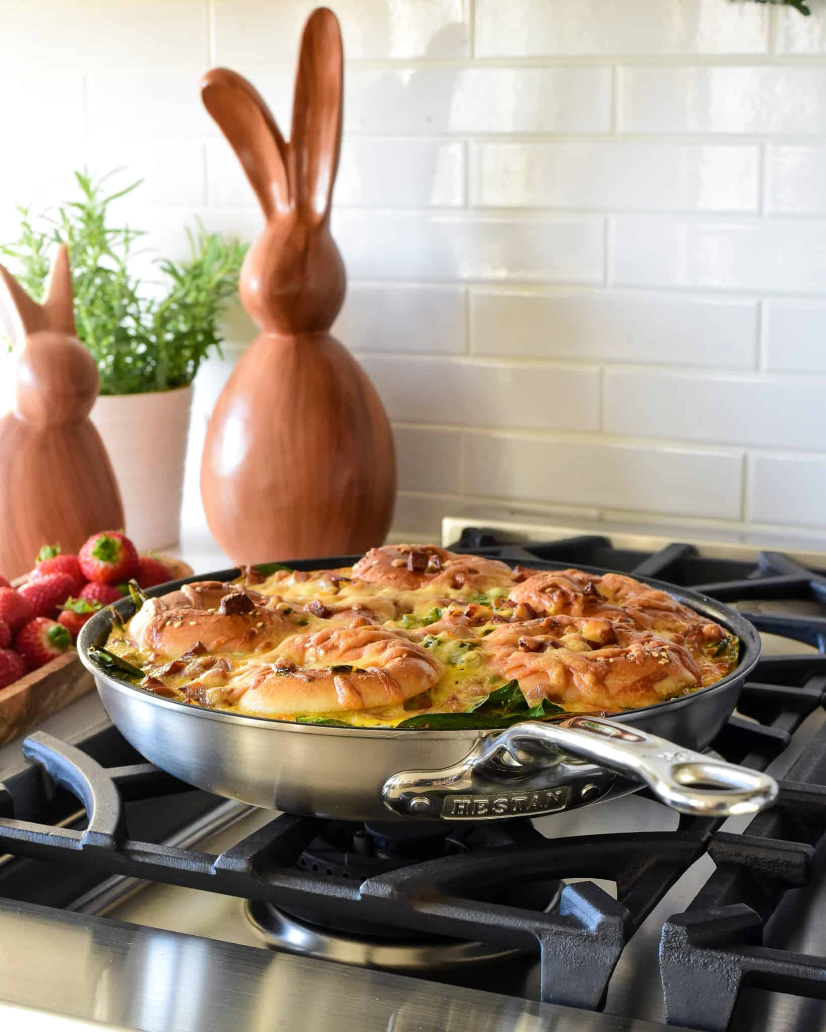 A skillet of a bagel bake on the oven with wooden Easter bunnies on the counter.