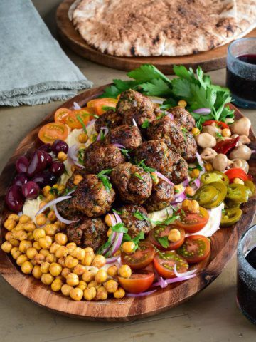 A platter of Loaded Hummus with Air Fryer Harissa Sausage Balls with a selection of fresh and pickled vegetables and herbs.
