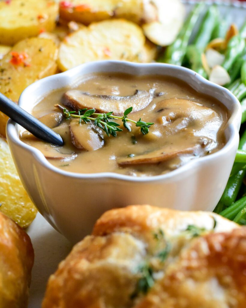 A bowl of Marsala mushroom sauce surrounded by individual ground beef wellingtons.
