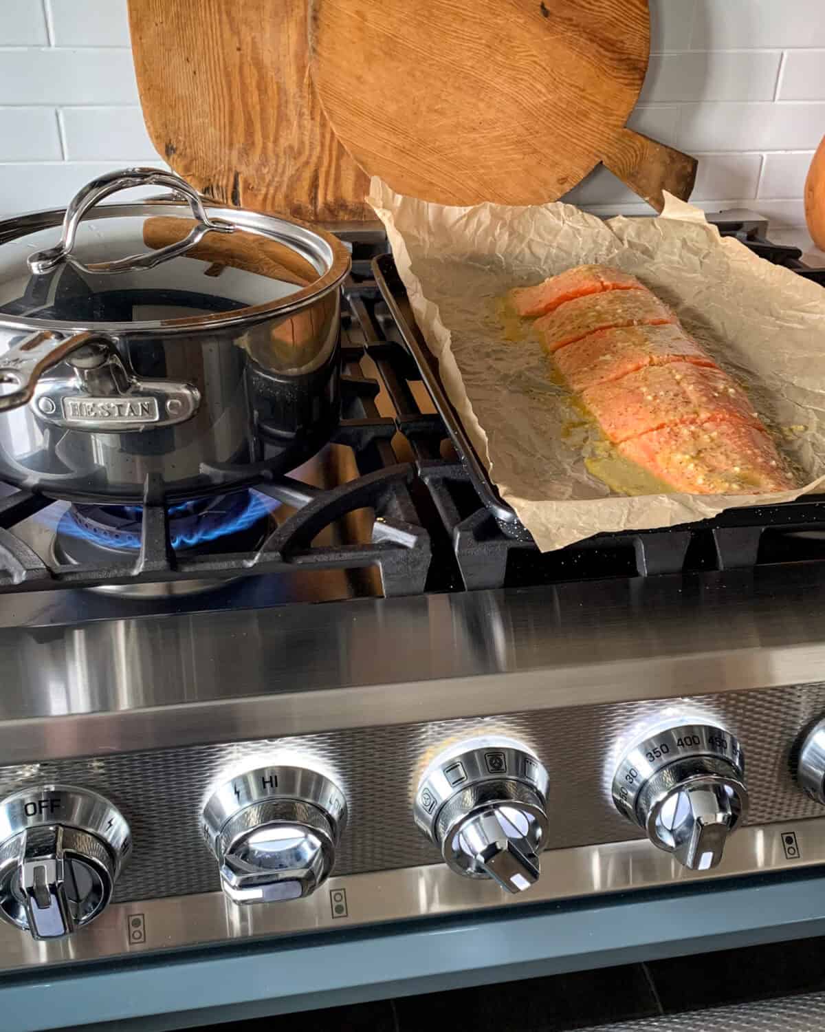 On the top of a range is a pot boiling potatoes and a sheet pan with a portioned Coho salmon ready to get roasted.