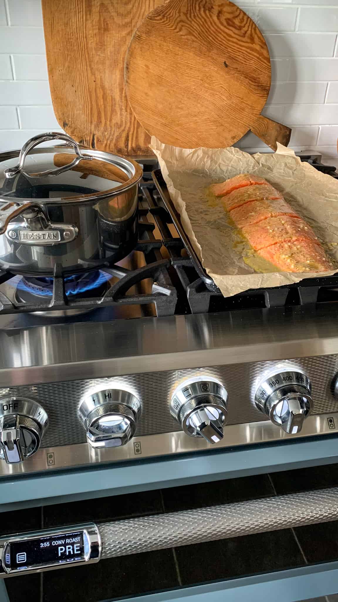 On the top of a range is a pot boiling potatoes and a sheet pan with a portioned coho salmon ready to get roasted. 