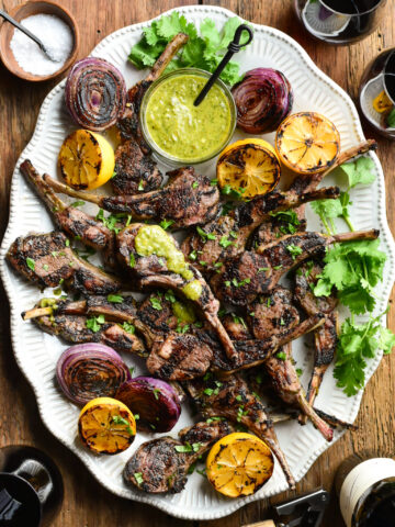 A platter of Charred Green Onion-Jalapeno-Lemon Lamb Chops with sauce, grilled onions and lemons.