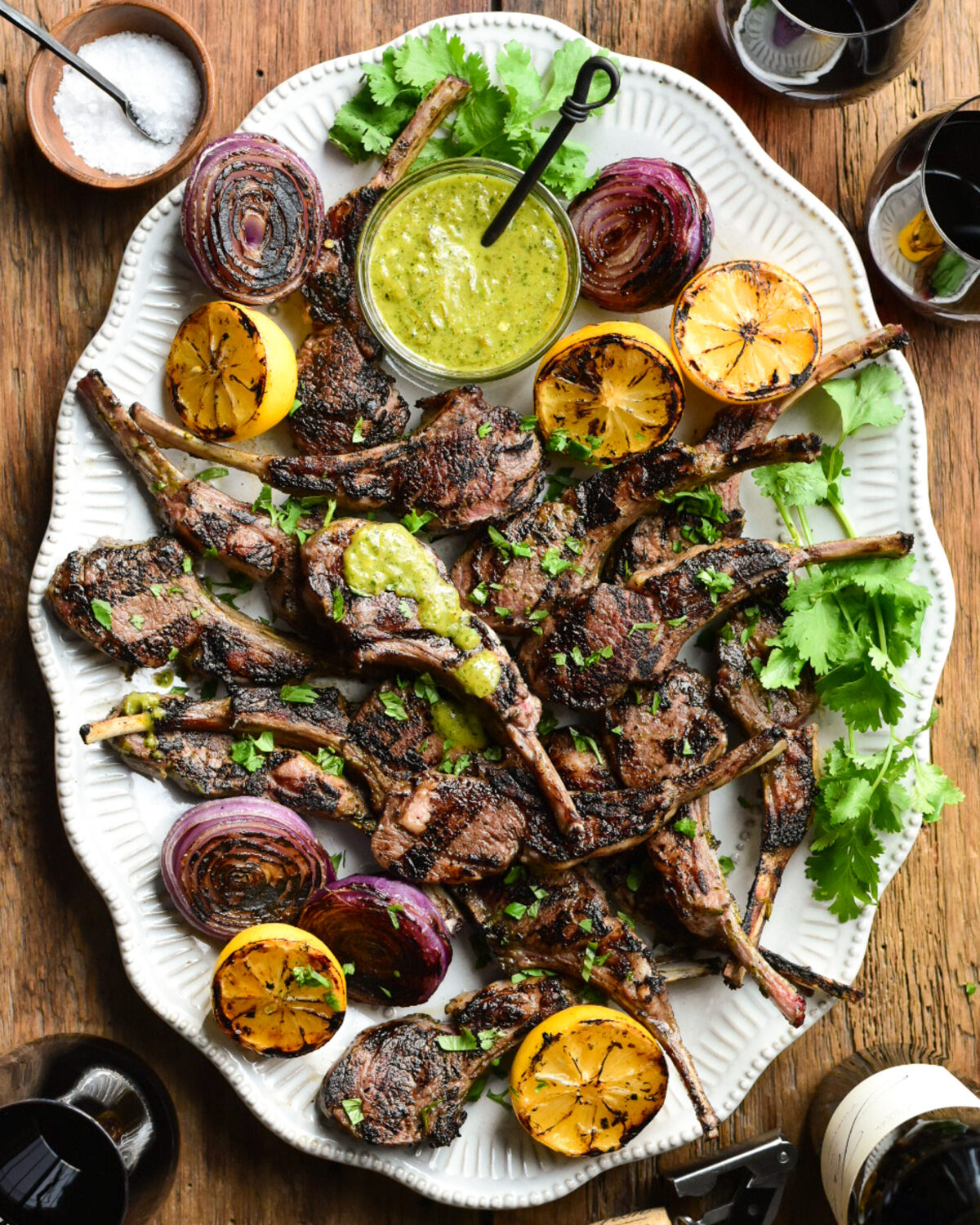 A platter of lamb chops with a green sauce and charred lemons and onions.