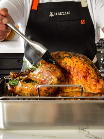 A side shot of a golden turkey getting based in roaster.