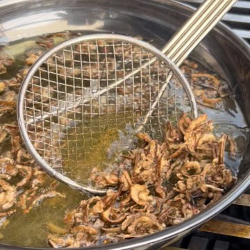 Shallots getting fried in a skillet of oil.