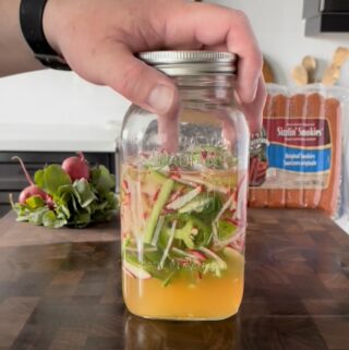 A mason jar with sliced vegetables in a pickling solution.