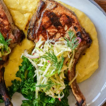A platter of creamy polenta served with pork chops and apple slaw.