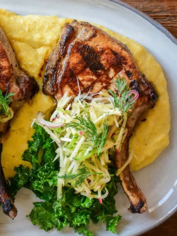 A platter of creamy polenta served with pork chops and apple slaw.