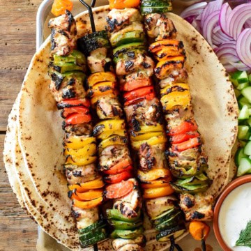 Four colourful grilled chicken and vegetable skewers served with pita.
