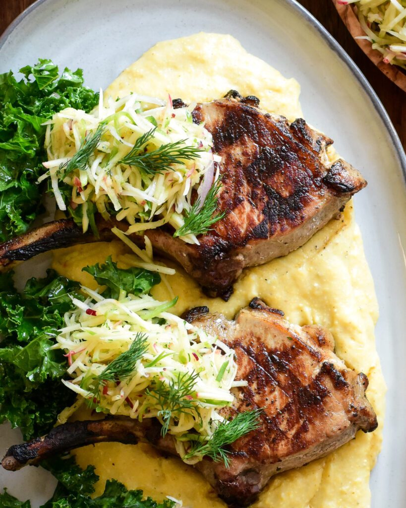 A close up of two pork chops & apple slaw on a bed of creamy polenta.