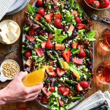 A top down image of a large Strawberry, Asparagus and Rhubarb Salad with dressing being poured on the salad.