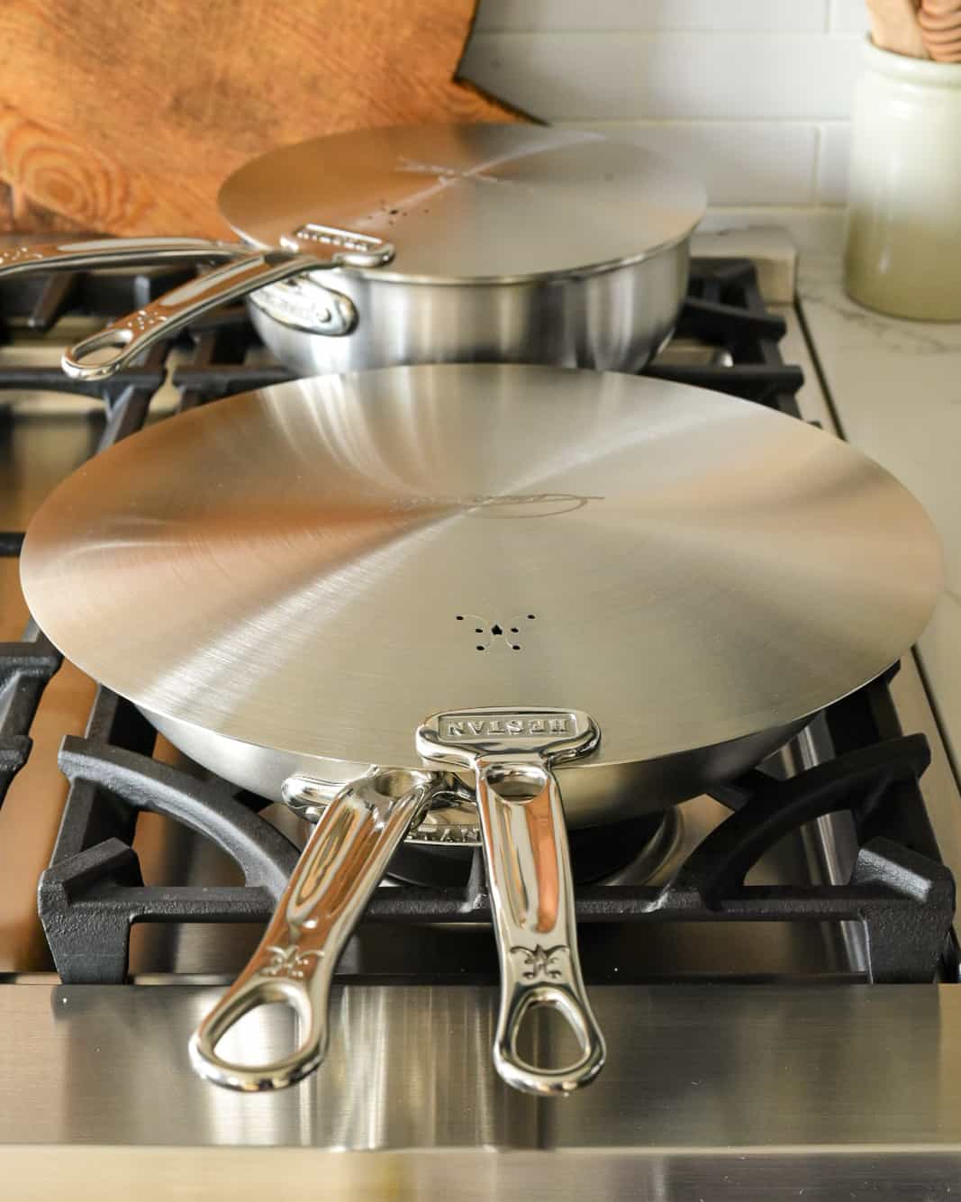 A skillet and a saucepan on a range each covered with a universal lid.