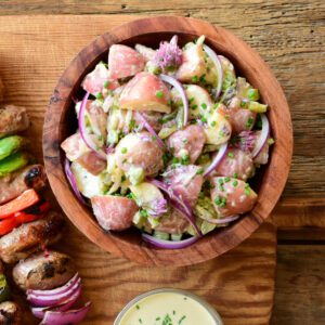 A chunky potato salad with pickles, celery, red onions and garnished with chives and chive blossoms in a wooden bowl.
