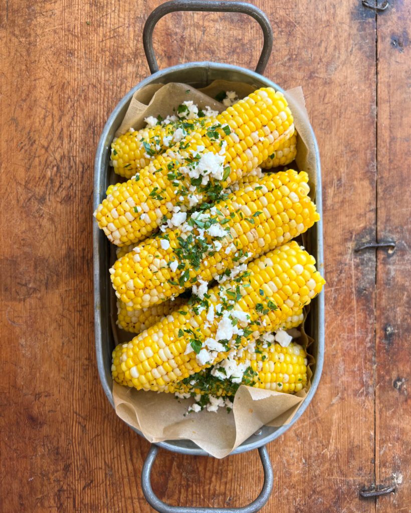 A pile of corn topped with a chili-lime butter, feta and cilantro in a galvanized tray.