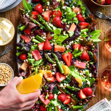 A colourful strawberry, asparagus and rhubarb salad. Dressing is getting poured over it.