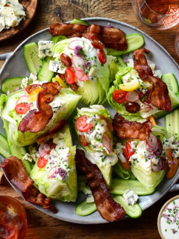 A large wedge salad with six lettuce wedges topped with dressing, tomatoes and pieces of bacon.