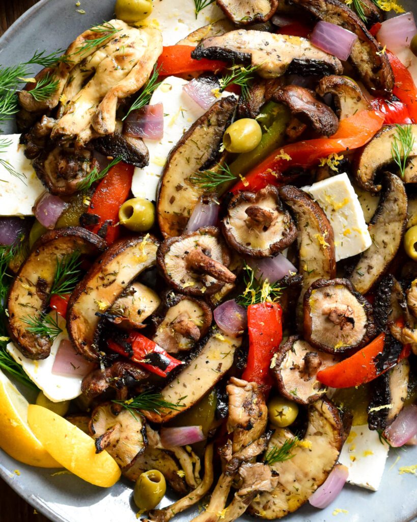 A close up of a round platter of Mediterranean Grilled Mushroom Salad  with peppers, olives and feta cheese.