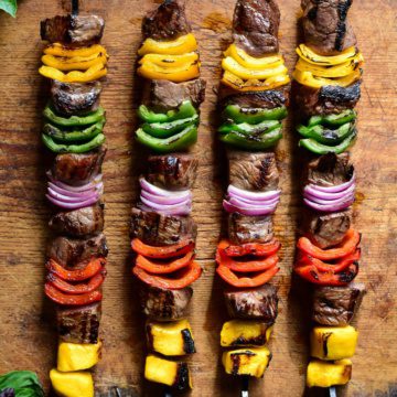 Four grilled beef skewers with alternating pieces of mango, peppers and onions.